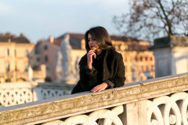 beautiful Italian girl with red dress and black jacket on the bridge in the square in Padua. High quality photo