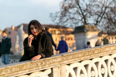 beautiful Italian girl with red dress and black jacket on the bridge in the square in Padua. High quality photo