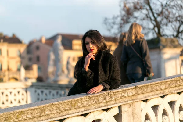 beautiful Italian girl with red dress and black jacket on the bridge in the square in Padua. High quality photo