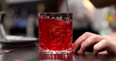 Barmen kırmızı alkollü bir kokteyl hazırlıyor. Malzemeler karıştırılıyor.
