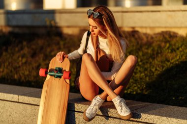 Gün batımında şehirde uzun bir sörf tahtasıyla oturan genç kadın..