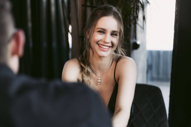 Genç bir kadın kocasıyla restoranda buluşurken gülümsüyor..