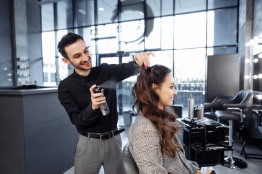 Genç, neşeli bir usta kadınların saçlarını spreyle düzeltir..