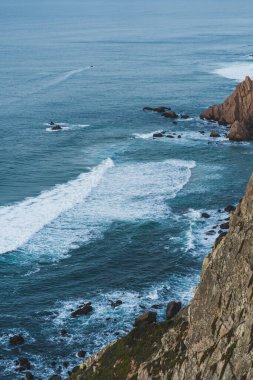 Mavi dalgalı kayalık sahil.