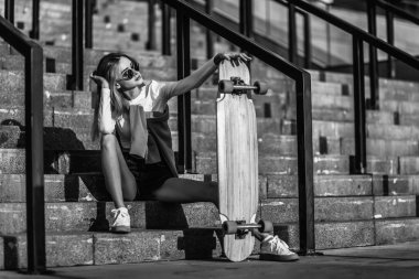 Güneş gözlüklü, merdivenlerde oturan, uzun tahtalı hoş bir genç kadın. Sıradan stil