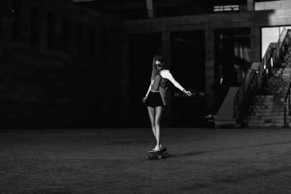 Frau auf einem Skateboard in der Stadt. Schöne kontrastreiche Schwarz-Weiß-Aufnahme einer Frau, die durch die Stadt reitet. — Stockfoto