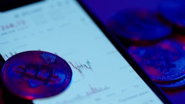 Bitcoin chart on mobile phone. Neon light falls on bitcoin coin. High quality 4k footage