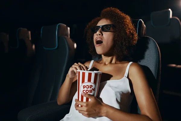 A young woman in 3D glasses is watching a movie enthusiastically. Popcorn in hands. High quality photo