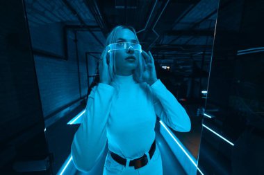 A blonde in neon glasses who is in a room with blue light. High quality photo