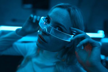 Neon mavi ışık fütüristik cam gözlük takan genç bir kadının üzerine düşüyor. Yüksek kalite fotoğraf