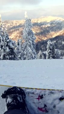 Dağların tepesinde gün batımını izleyen snowboardcu.