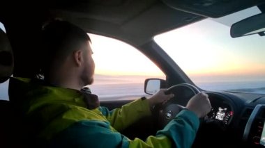 Adam puslu havada gün doğumunda araba sürüyor.