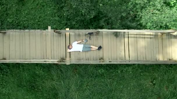 Patika köprüsünde uzanan adam yukarı çıkıyor. — Stok video