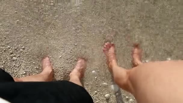 Punto de vista hombre y mujer pies en la playa bañado por las olas del mar — Vídeo de stock
