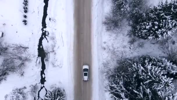Вид с воздуха на автомобиль, движущийся вперед по заснеженной дороге — стоковое видео
