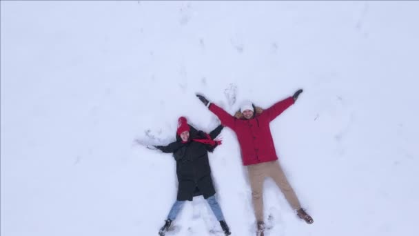 Par man och kvinna har kul på snöfält gör snö ängel — Stockvideo