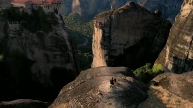 Kayalıklarda oturan iki gezgin, Yunanca meteora şablonlarına bakıyor.