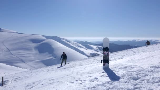 Сноуборд перед людьми, поднимающимися на лыжном склоне — стоковое видео