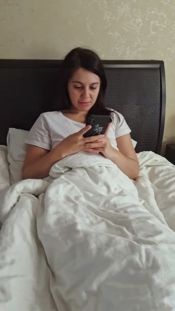 Wanita berbaring di tempat tidur surfing internet di telepon — Stok Video