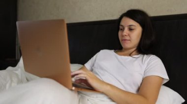 gülümseyen kadın yatakta dizüstü bilgisayar üzerinde çalışan