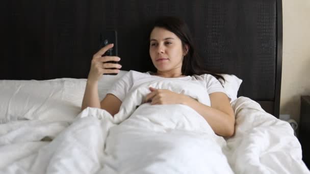 Wanita berbaring di tempat tidur surfing internet di telepon — Stok Video