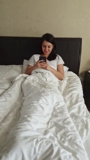 Nő feküdt az ágyban szörfözés interneten a telefonon — Stock videók