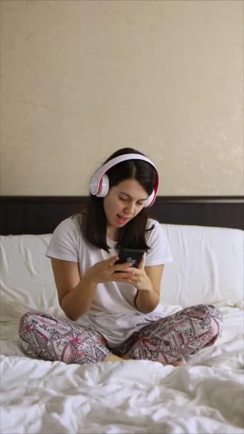 Žena poslouchající na posteli hudbu se sluchátky — Stock video