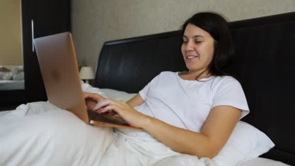 Wanita tersenyum bekerja pada laptop di tempat tidur — Stok Video