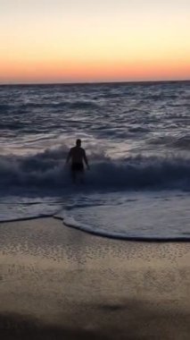 Gülümseyen adam fırtınalı denizde gün batımında yüzecek.