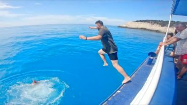 Lefkada, Yunanistan - 04 Eylül 2021: adam açık deniz suyunda tekneden atlıyor