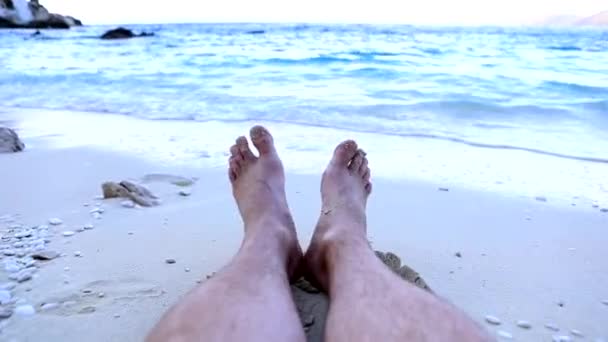 Punto de vista hombre piernas tendidas en la playa mar olas en el fondo — Vídeo de stock