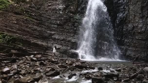 Симпатичная туристка, стоящая перед большим водопадом — стоковое видео