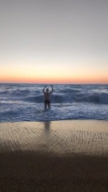 Gülümseyen adam fırtınalı denizde gün batımında yüzecek.