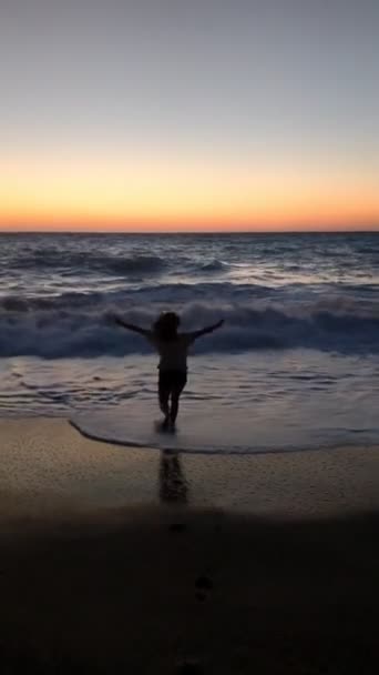 Młoda kobieta biegnie do morza ciesząc się widokiem na zachód słońca — Wideo stockowe