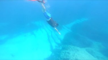 Dalgıç maskesi ve yüzgeçleriyle suyun altında yüzen bir adam.