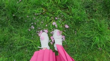 Çimlerin üzerinde duran pembe etekli kadın sakura çiçekleriyle