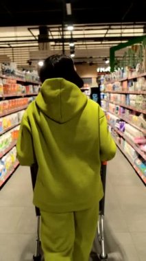 Tıbbi maskeli bir kadın elinde tıbbi maskeyle marketin önünden geçiyor.