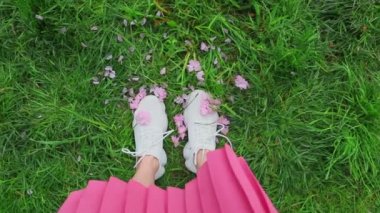 Çimlerin üzerinde duran pembe etekli kadın sakura çiçekleriyle