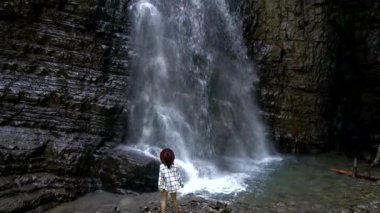 Güzel yürüyüşçü kadın büyük şelalenin önünde duruyor.