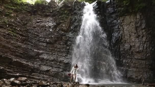 Bonita mujer excursionista de pie frente a una gran cascada — Vídeo de stock