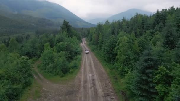 Vista aérea do carro SUV movendo-se pela estrada caminho em montanhas nublado tempo chuvoso nebuloso — Vídeo de Stock