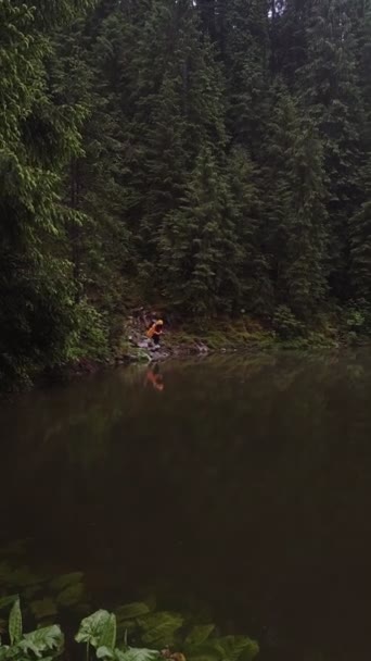 Жінка в жовтому плащі фотографує на телефоні лісового озера — стокове відео