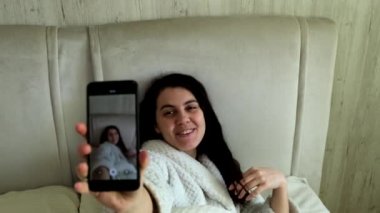 Mutlu blogcu yatakta yatarken telefonda video çekiyor.