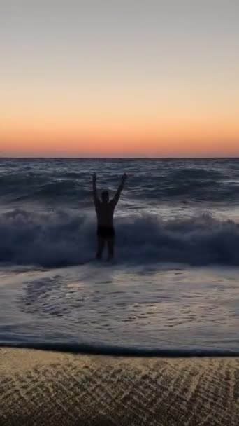 Улыбающийся человек собирается искупаться в бурном море на закате — стоковое видео