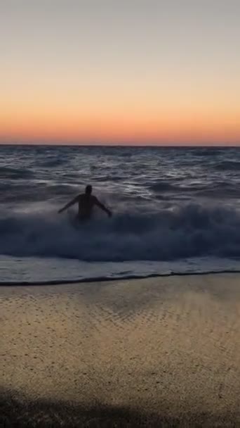 Uomo sorridente che va a nuotare nel mare tempestoso al tramonto — Video Stock
