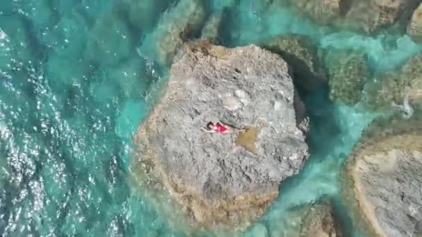 澄んだ青い海の岩の上に寝そべっている女性の — ストック動画