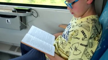 Gözlüklü küçük çocuk tren yaşam tarzında kitap okuyor.