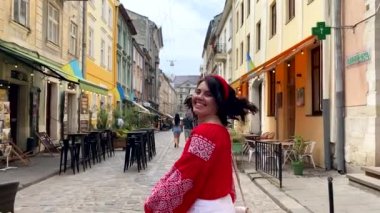 Ukrayna 'nın Lviv caddesinde yürüyen kırmızı işlemeli gömlekli mutlu güzel kadın.