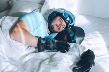 Kar kayağı google 'ı ve kaskla yatakta kar dağlarını düşleyen bir adam.