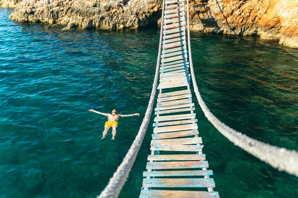 Adam Arkada Deniz Suyunda Yüzüyor Kayalık Sahili Asma Köprüsü Olan — Stok fotoğraf